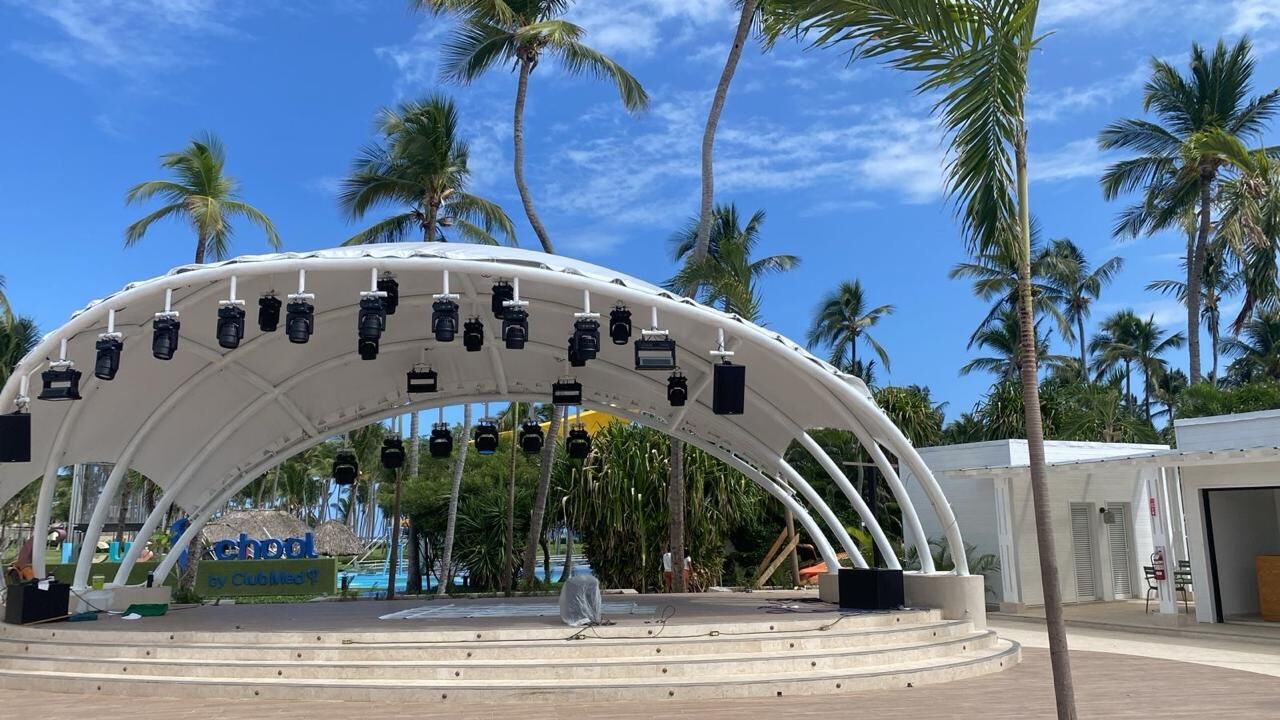 Escenario con cubierta textil en arco frente al mar, rodeado de palmas