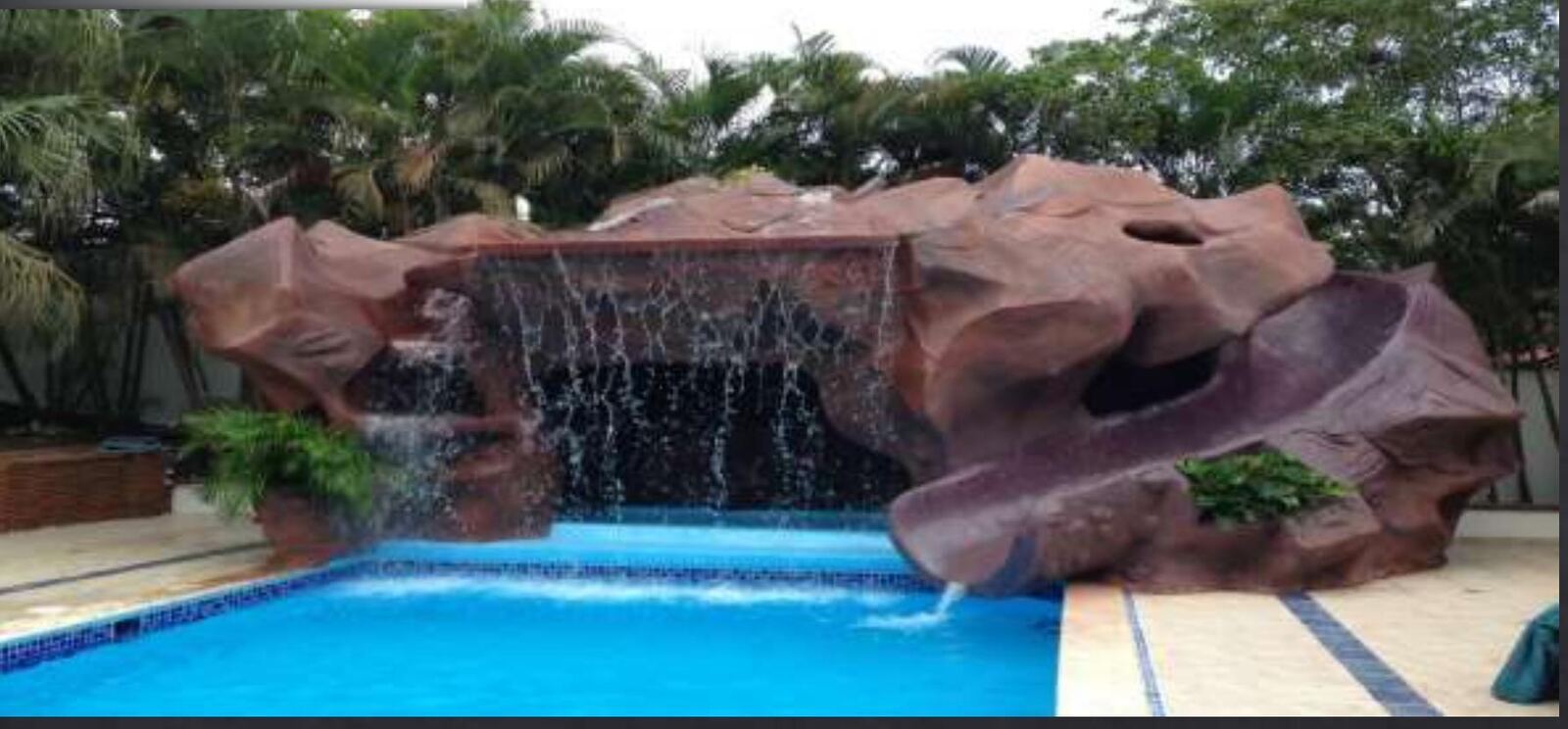 Roca artificial con cascada y tobogán sobre piscina
